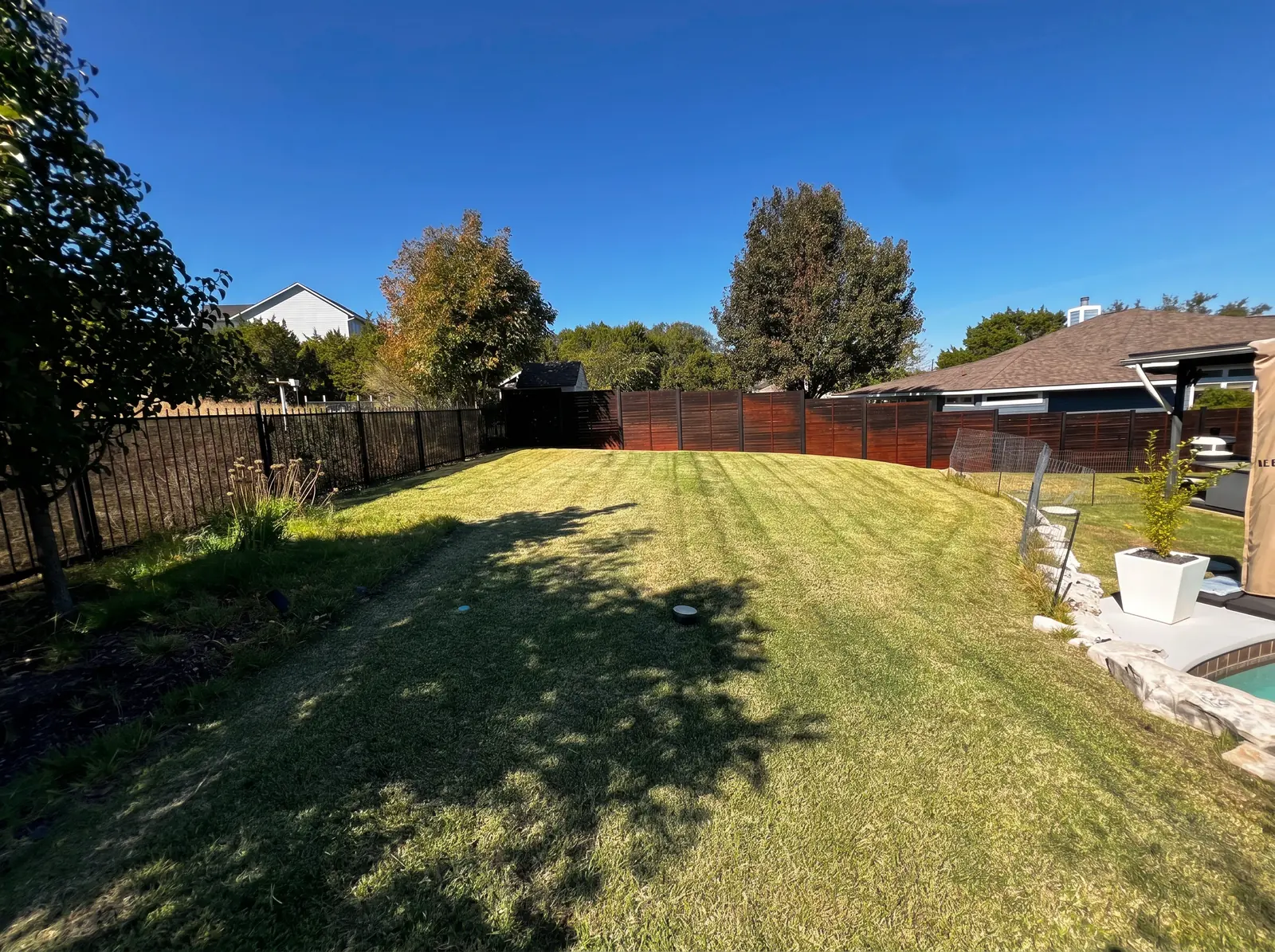 Freshly mowed backyard with visible lawn stripes beside a patio and fence.