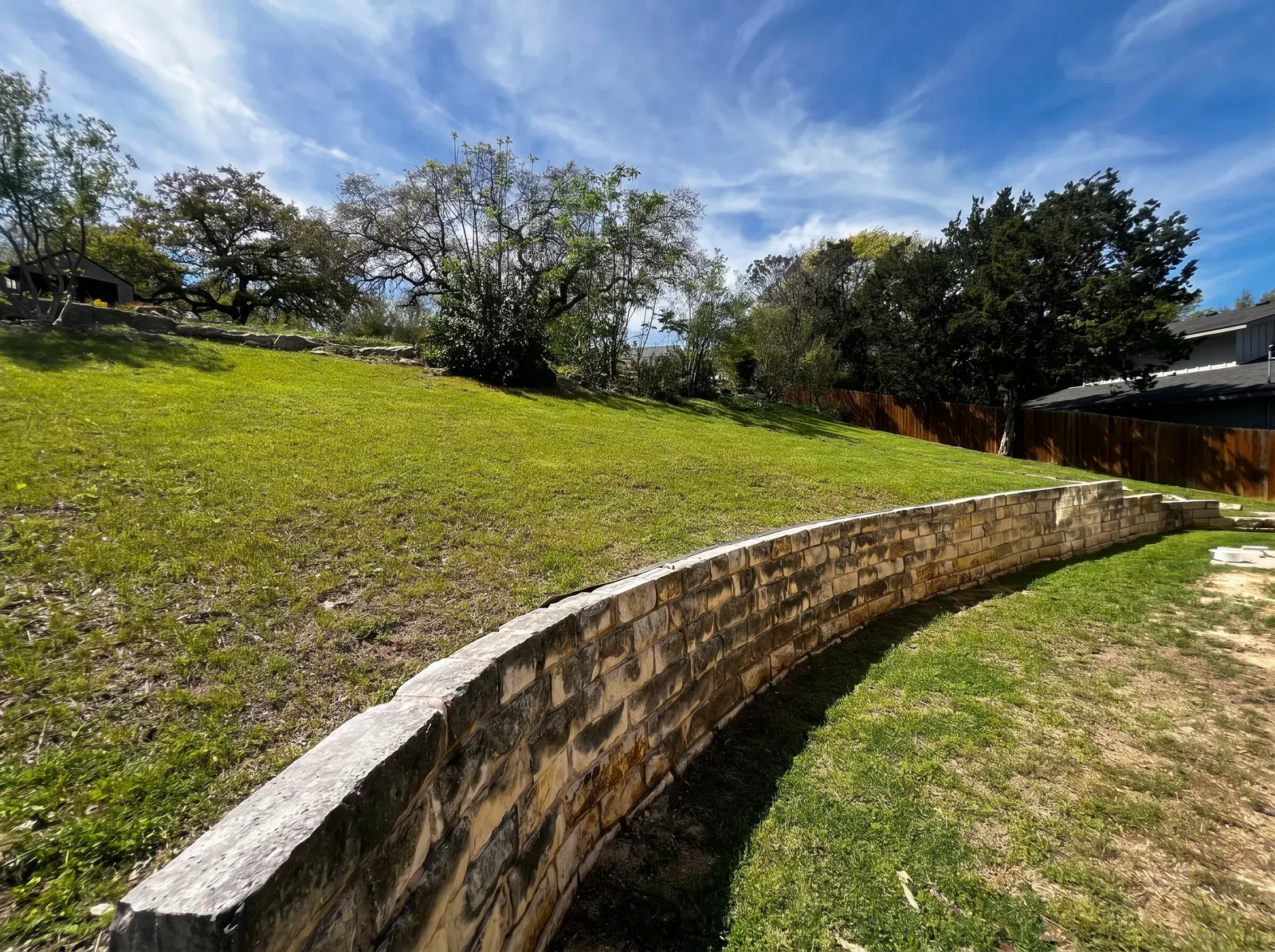Sloped lawn above a long stone retaining wall under a blue sky.