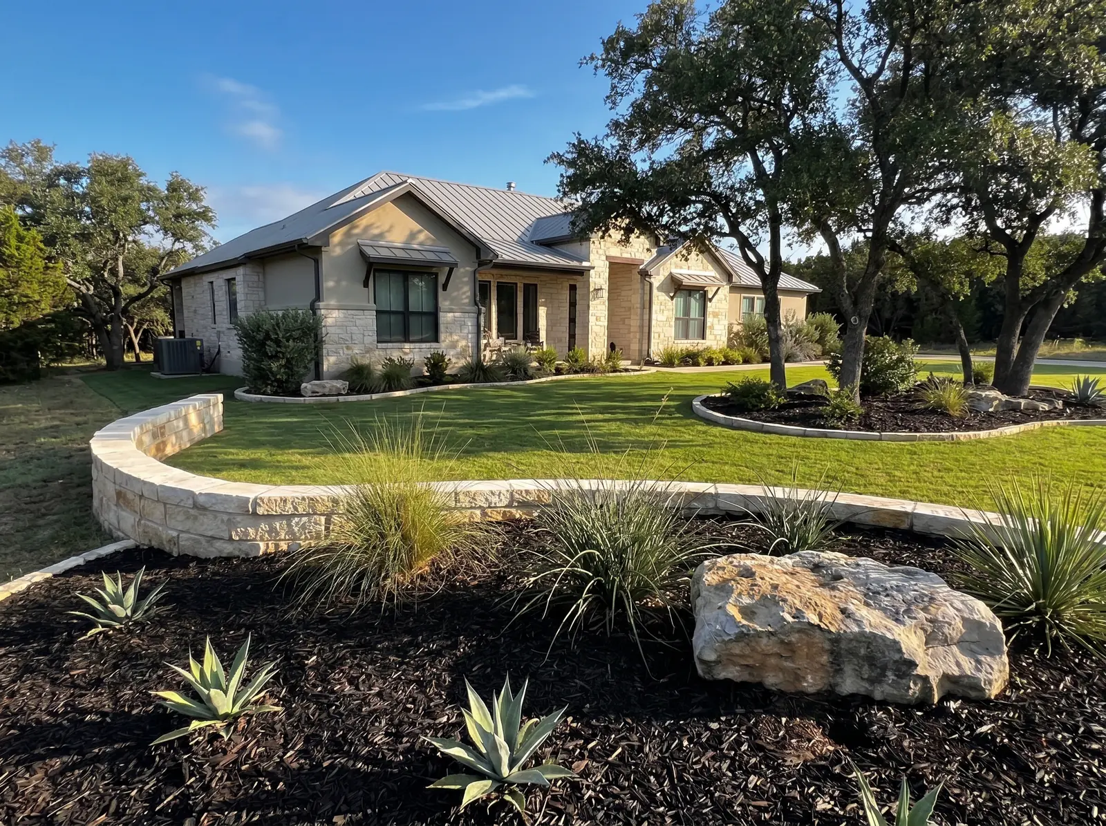 Front landscape with curved limestone border, agave plants, ornamental grasses, and mowed lawn.